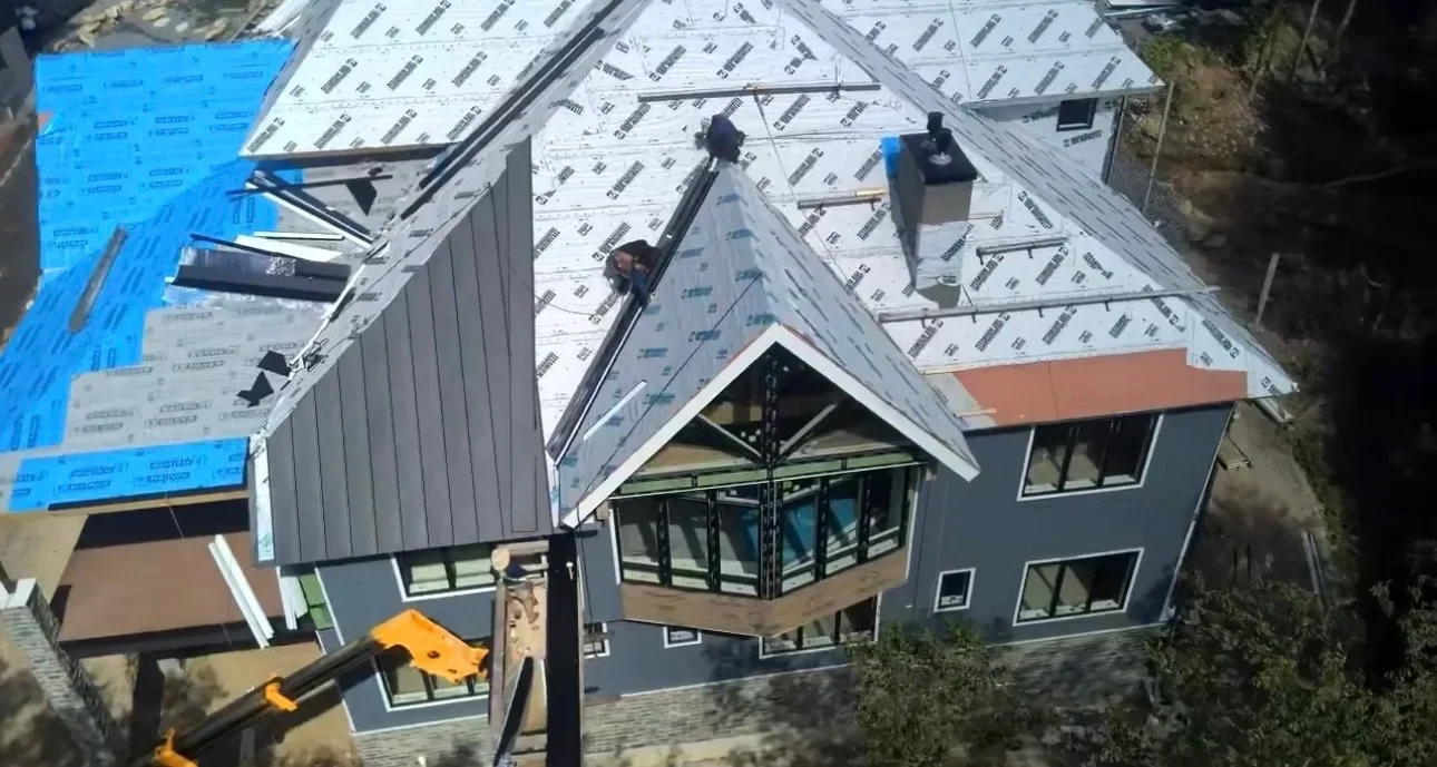 Aerial view of residential roof with synthetic underlayment, metal flashing, and standing seam roofing installation in progress