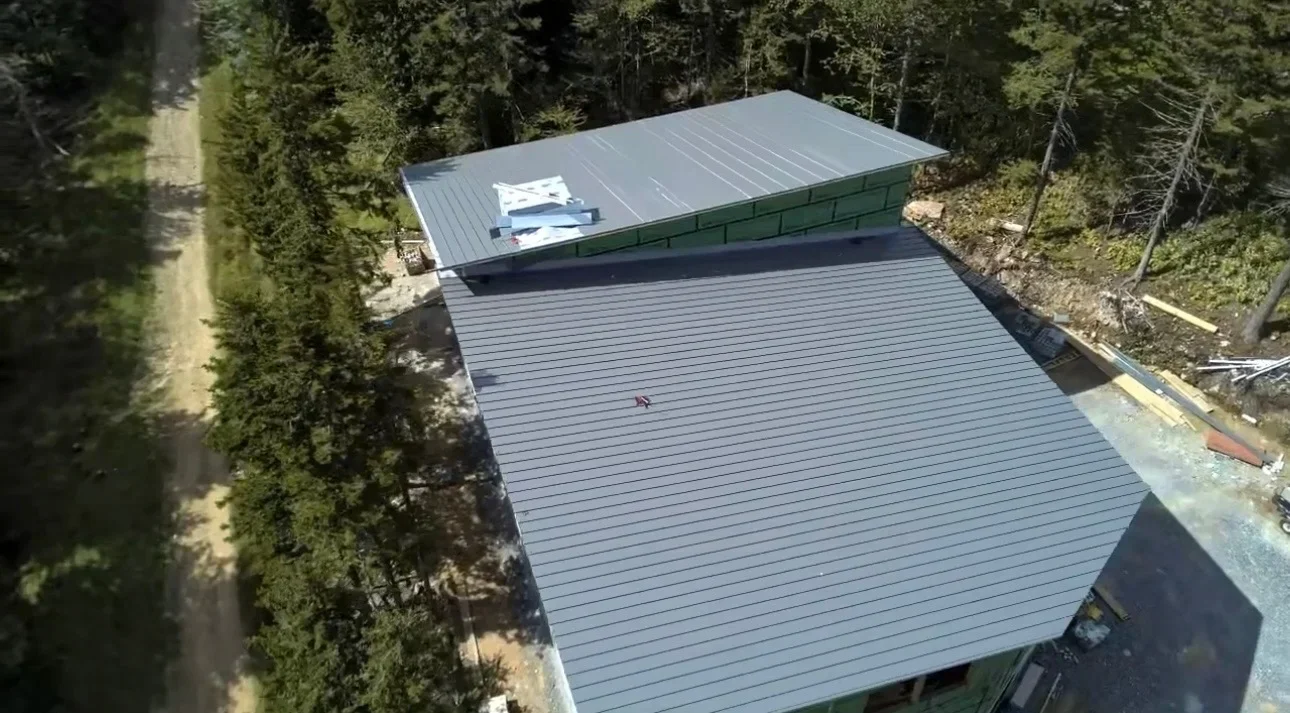 Gray standing seam metal roof with green trim and guttering on residential structure